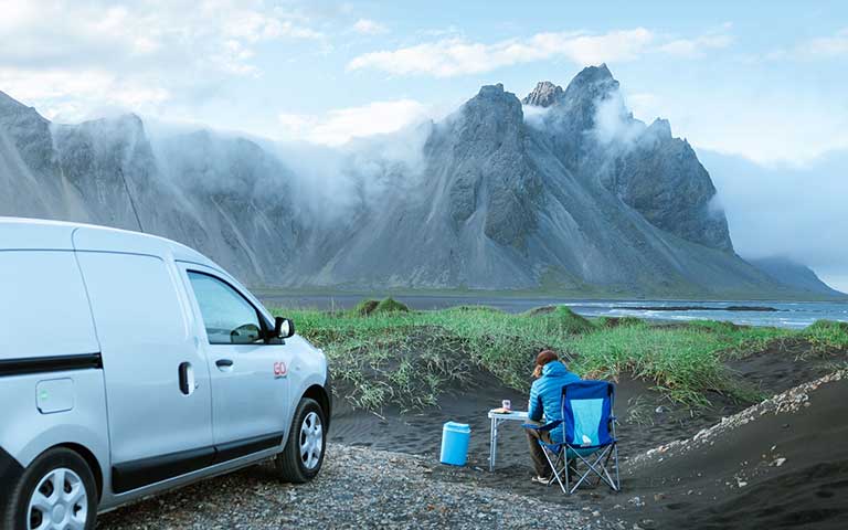 Man having lunch and sitting by a campervan, camping in Stokksnes
